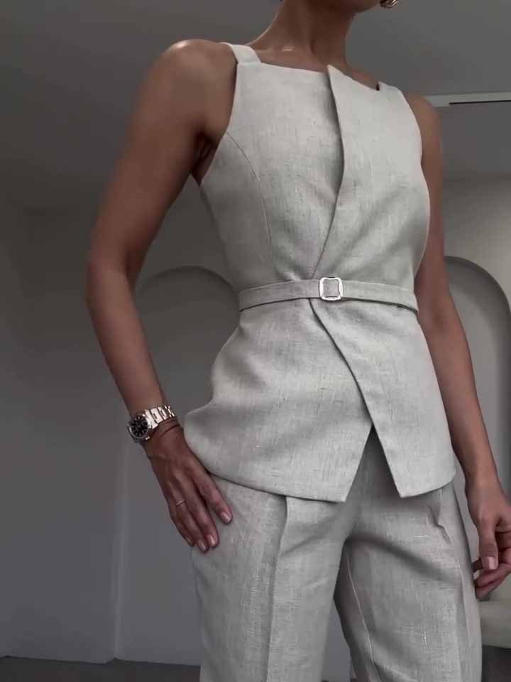 Person wearing a light gray sleeveless blazer and pants set against a neutral background