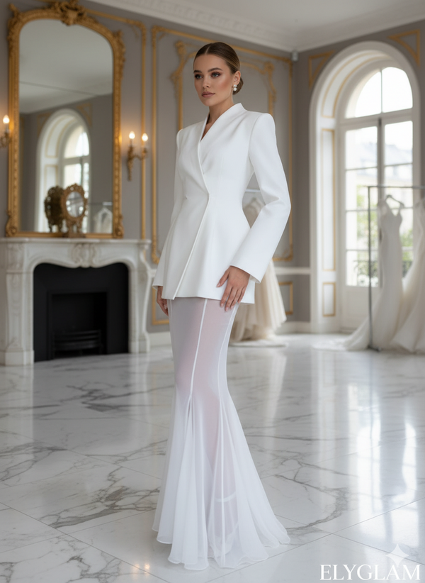 Woman in a white bridal outfit standing in an elegant room with marble floors and large mirrors.